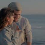 A couple enjoys a conversation by the sea on a windy day, captured in a serene moment.